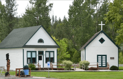 A quaint library building next to a small church, surrounded by trees and greenery.