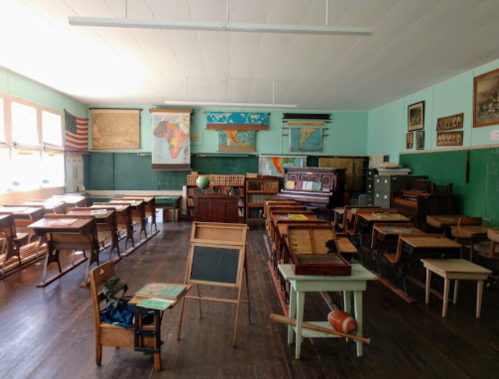 A vintage classroom with wooden desks, maps on the walls, and an old piano, evoking a historical educational setting.