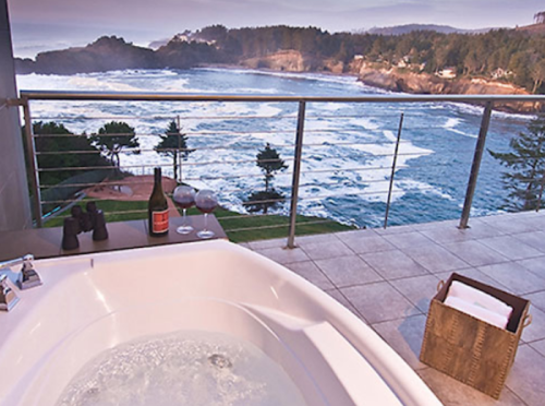 A luxurious bathtub on a balcony overlooking a scenic ocean view with waves and trees in the background.