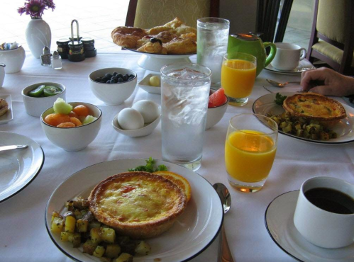 A breakfast table with eggs, fruit, pastries, drinks, and a variety of dishes arranged neatly.