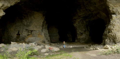 A panoramic view of a dark cave entrance with rocky walls and a person standing in the center.