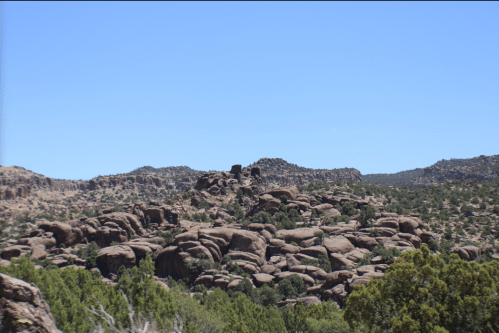 A rocky landscape with large boulders and sparse greenery under a clear blue sky.