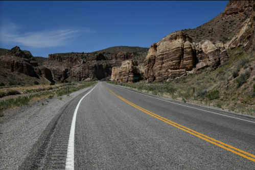 A winding road stretches through rocky terrain under a clear blue sky, surrounded by rugged cliffs and sparse vegetation.