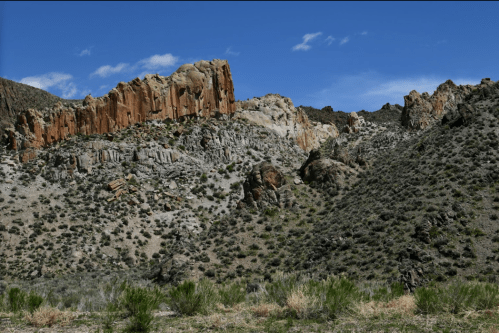 Rocky cliffs rise against a clear blue sky, surrounded by sparse vegetation and rugged terrain.