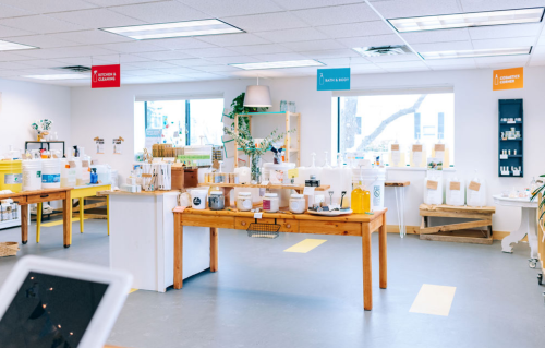 Bright, spacious shop interior with wooden tables displaying various bottles and containers for bath and body products.