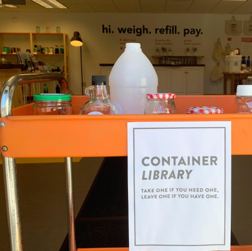 A cart with various containers and a sign reading "Container Library: Take one if you need one, leave one if you have one."