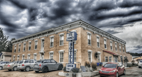 Historic St. James Hotel with a cloudy sky, surrounded by parked cars and greenery.