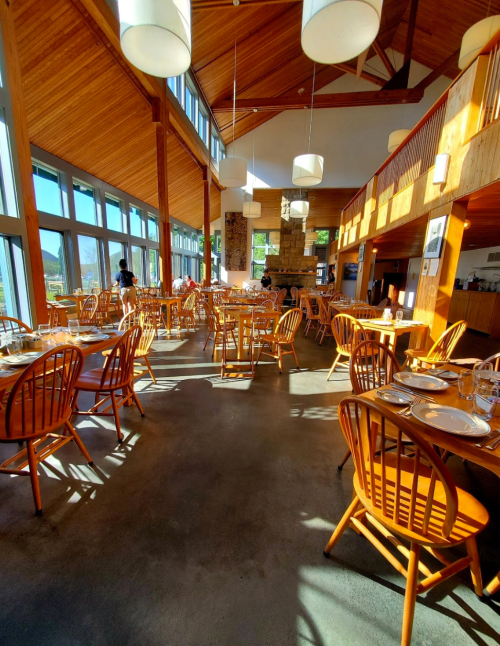 Bright, spacious restaurant interior with wooden decor, large windows, and empty tables set for dining.