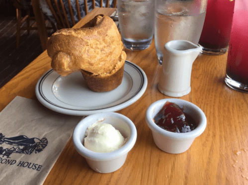 A golden brown popover with butter and jelly on a wooden table, accompanied by glasses of water and drinks.
