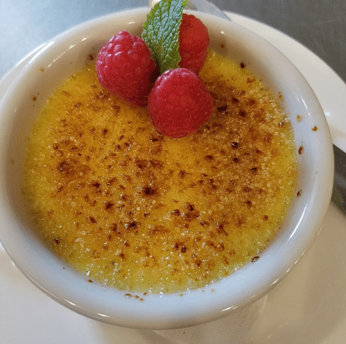 A creamy dessert topped with caramelized sugar, garnished with three raspberries and a mint leaf.