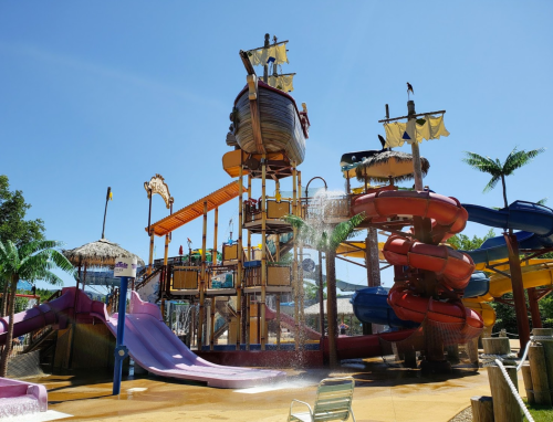 Colorful water park with multiple slides, a pirate ship structure, and palm trees under a clear blue sky.
