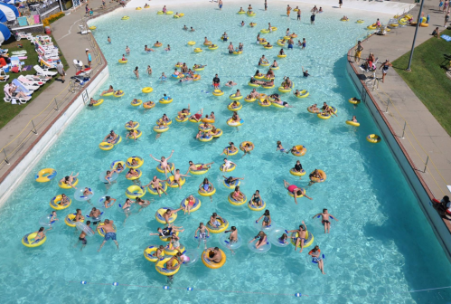 Aerial view of a crowded water park pool filled with people on yellow inner tubes enjoying the water.