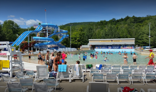 A busy water park with a large pool, water slides, and people enjoying the sun and swimming.
