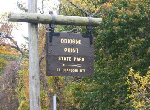Wooden sign for Odiorne Point State Park, indicating the Fort Dearborn site, surrounded by trees in autumn.