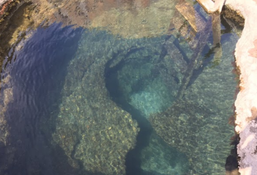 Clear blue water in a natural pool with rocky edges and visible underwater formations.