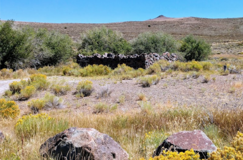 A rocky ruin surrounded by sparse vegetation and rolling hills under a clear blue sky.