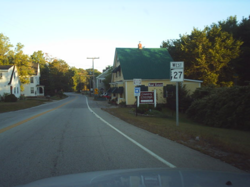 A winding road with a green-roofed building and a sign for Country Crossing Real Estate on the side.