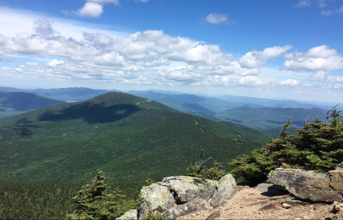 A panoramic view of green mountains under a blue sky with fluffy clouds, showcasing a serene natural landscape.
