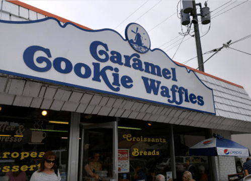 Sign for "Caramel Cookie Waffles" shop with outdoor seating and a cloudy sky in the background.