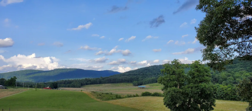 A scenic landscape featuring rolling hills, green fields, and a blue sky with fluffy clouds.