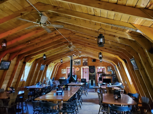 Cozy wooden interior of a restaurant with tables, ceiling fans, and rustic decor, featuring a warm, inviting atmosphere.