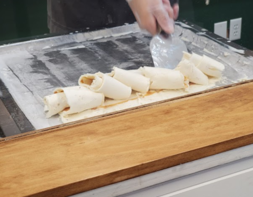 A person using a spatula to roll ice cream on a cold surface, creating rolled ice cream desserts.
