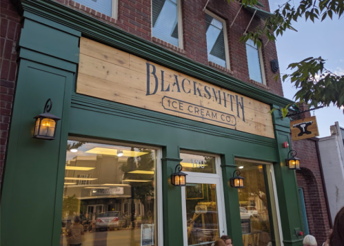 Exterior of Blacksmith Ice Cream Co. featuring a wooden sign and green trim, with lanterns and a nearby anvil sign.