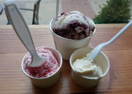 Three cups of ice cream: one with red swirl, one pink, and one white, all with plastic spoons on a wooden table.