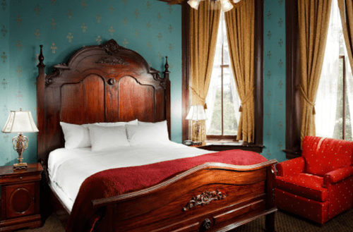 A cozy bedroom featuring a wooden bed, red accents, elegant curtains, and a comfortable armchair.