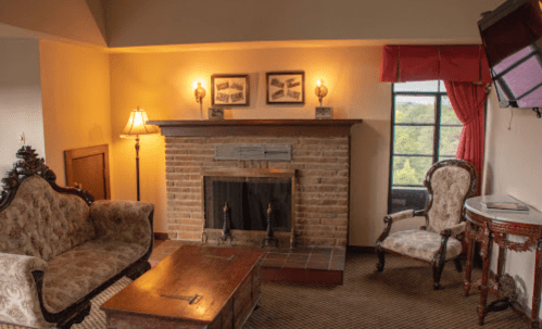 Cozy living room with a brick fireplace, vintage furniture, and large windows offering a view.