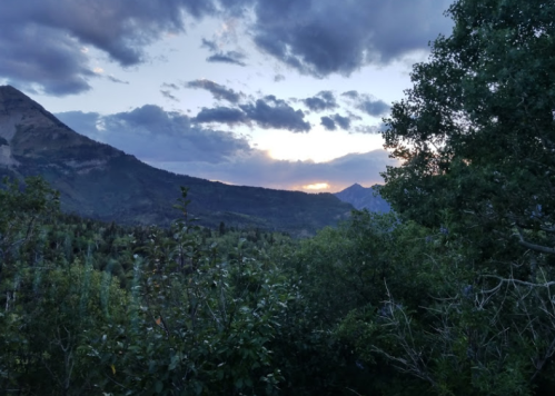 A scenic view of mountains and trees at sunset, with clouds scattered across the sky.