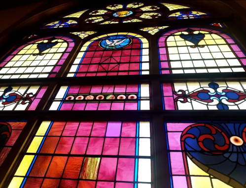 Colorful stained glass window featuring intricate patterns and a dove symbol at the top.