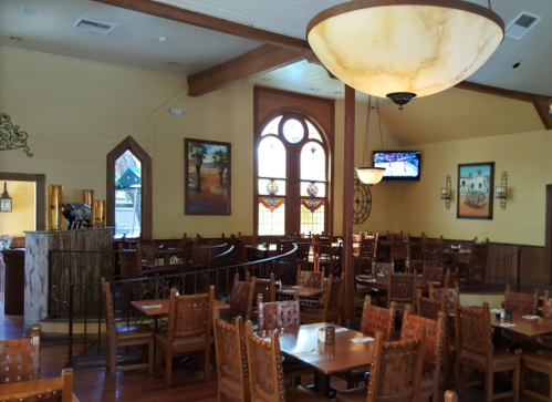 Interior of a restaurant featuring wooden tables, chairs, stained glass windows, and a large chandelier.