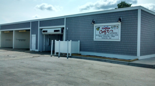 Exterior of a catering business with a sign displaying hours and services, featuring a gray shingle facade.