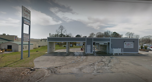 A car wash building with a sign, featuring multiple wash bays and a paved lot, under a cloudy sky.