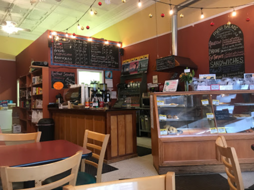 Cozy café interior with a counter, menu board, display case, and wooden tables, decorated with string lights.