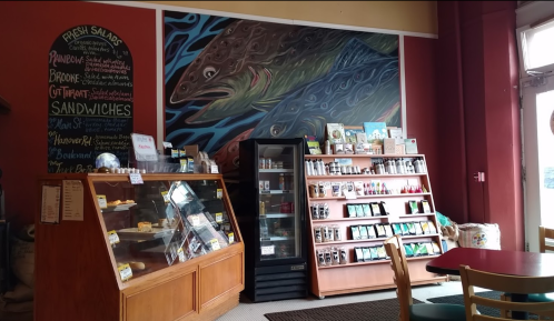 Interior of a café featuring a mural of fish, a display case with pastries, and shelves of drinks and snacks.