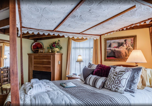 Cozy bedroom with a four-poster bed, decorative ceiling, fireplace, and warm lighting. Elegant decor and soft linens.
