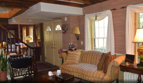 Cozy living room with a striped sofa, warm lighting, and wooden beams, featuring a staircase and decorative plants.