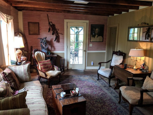 Cozy living room with vintage furniture, a rug, and a door leading to an outdoor space, adorned with decorative items.