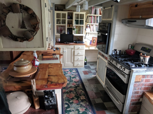 Cozy kitchen with wooden cabinets, a gas stove, and a desk area, featuring a colorful rug and various kitchen items.