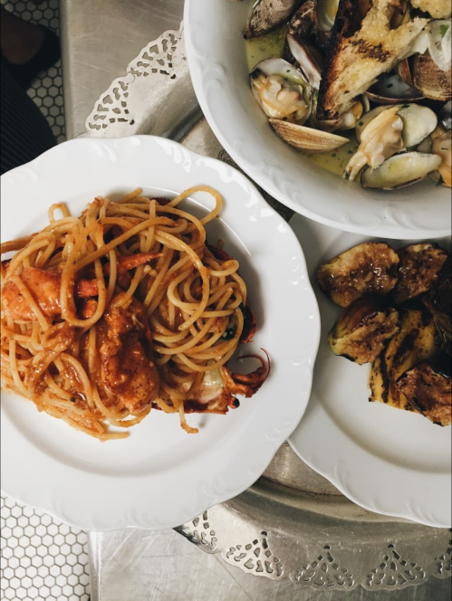 A plate of spaghetti with seafood, alongside a dish of clams and grilled vegetables on a decorative tray.