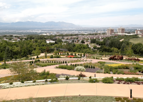 A scenic view of a landscaped garden with colorful flowers, overlooking a city and mountains in the background.