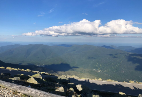 A panoramic view of green mountains under a blue sky with fluffy clouds, showcasing a serene landscape.