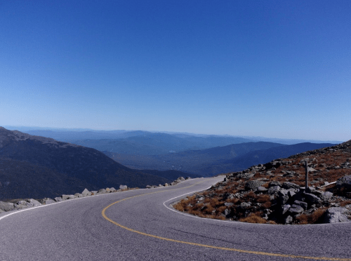 Winding road through rocky terrain with expansive mountain views under a clear blue sky.