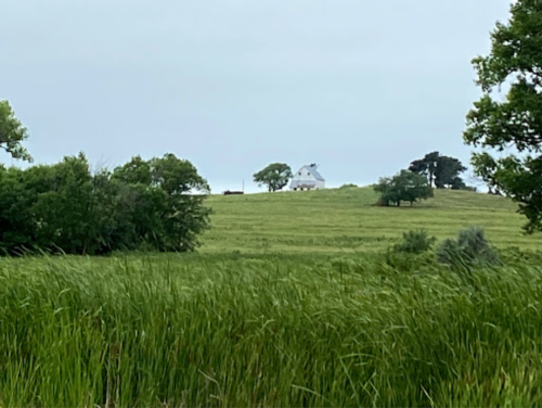 A white barn on a grassy hill, surrounded by trees under a cloudy sky.