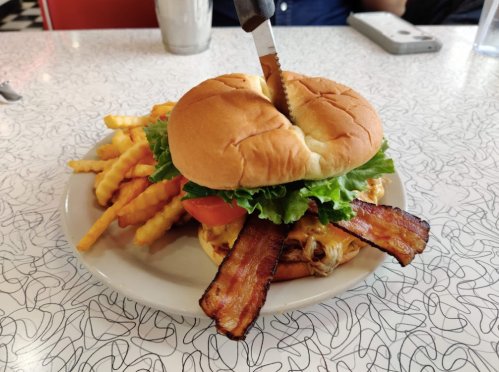 A sandwich with lettuce, tomato, and bacon, served with crinkle-cut fries on a retro-style table.