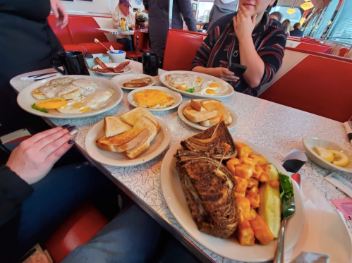 A diner table with three plates of breakfast food, including eggs, toast, and a large portion of corned beef hash.