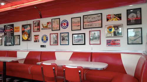 Retro diner interior featuring red booths and a wall adorned with vintage posters and framed memorabilia.
