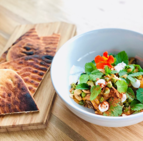 A bowl of colorful salad with herbs and toppings, accompanied by toasted flatbreads on a wooden board.